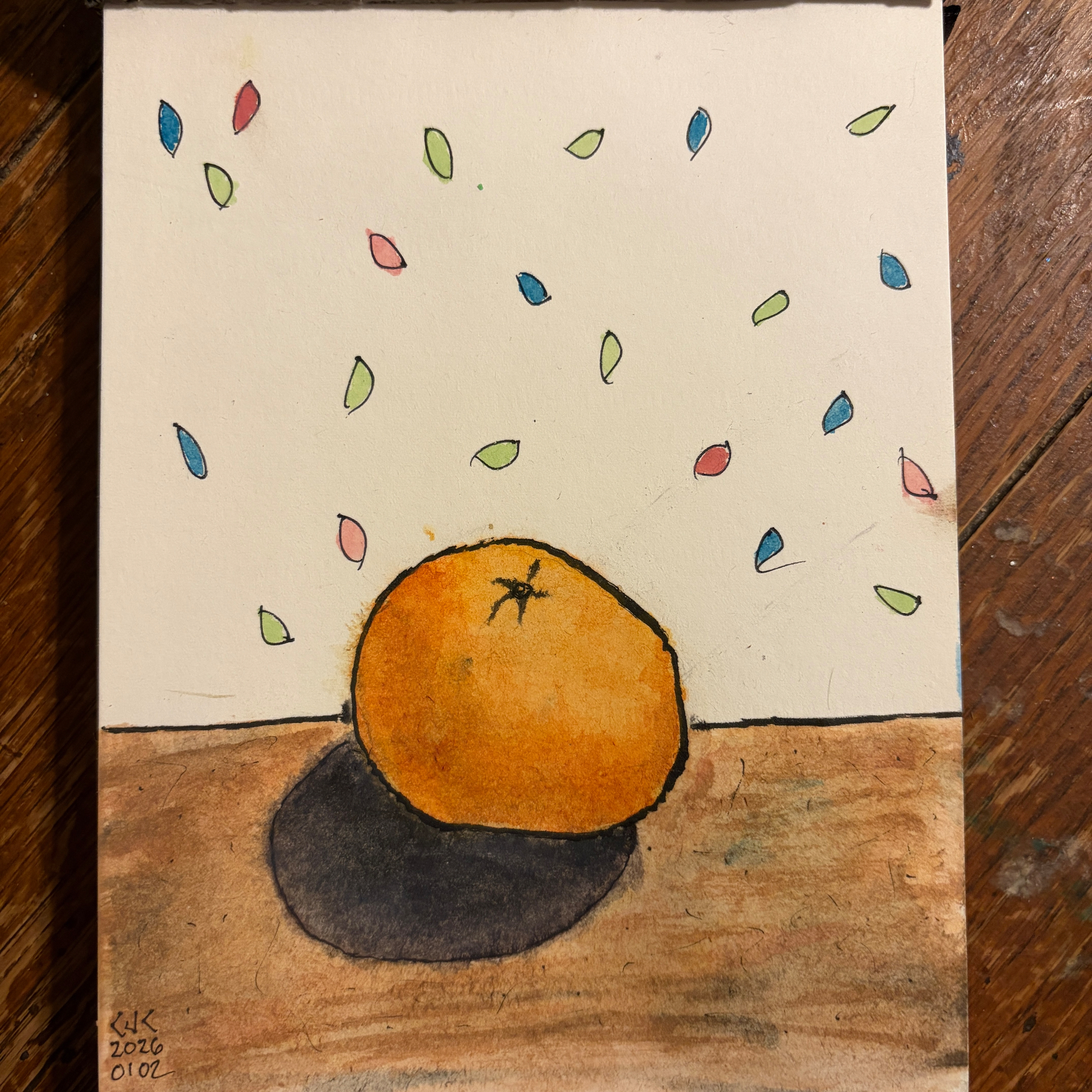 A watercolor painting shows an orange on a table with colorful leaves floating above it.